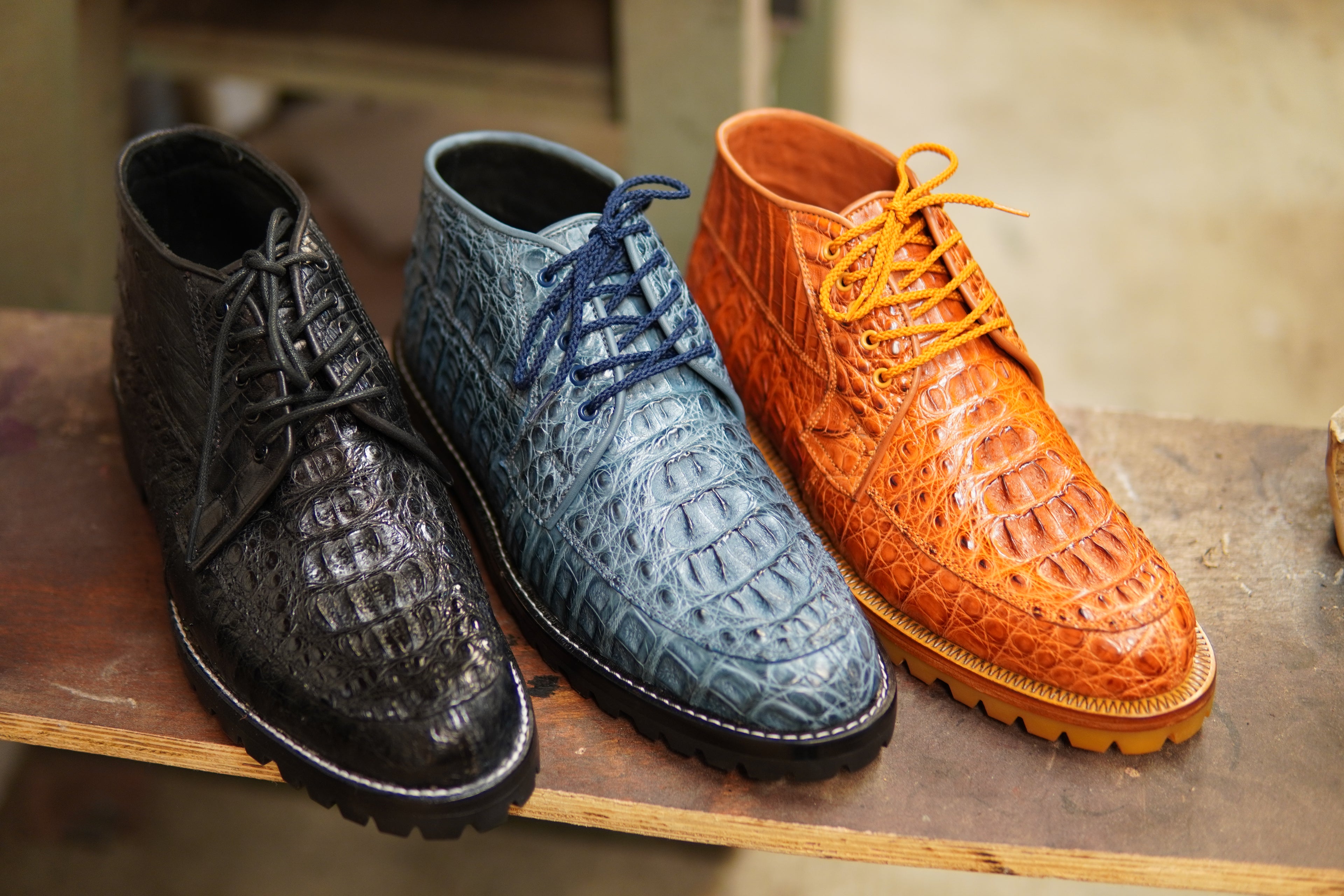 Three pairs of textured dress shoes in black, blue, and orange on a wooden surface.