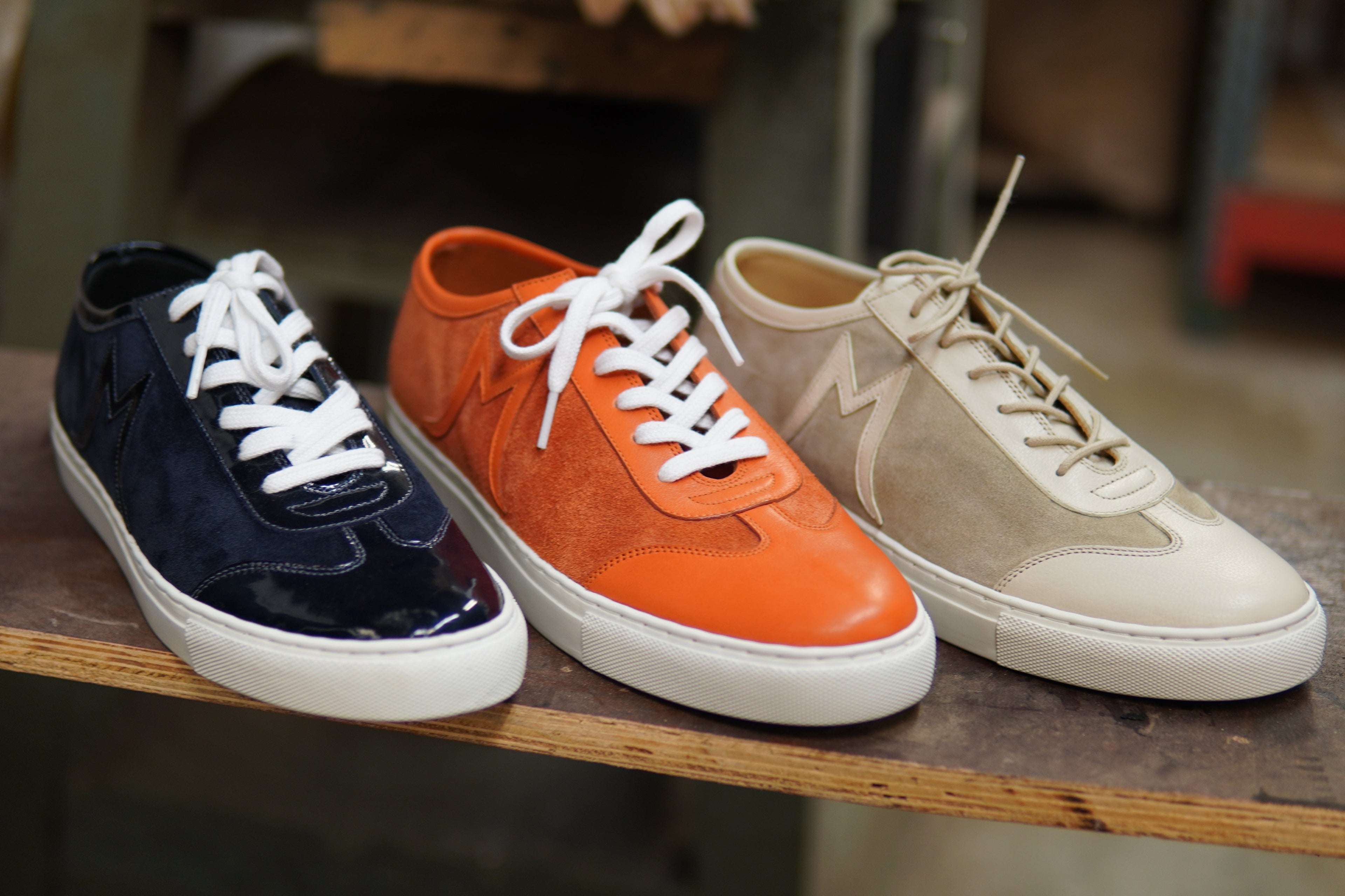 Three sneakers in black, orange, and beige on a wooden surface.